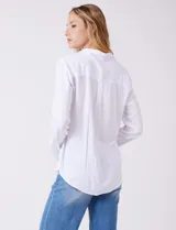 Camisa blanca de rayón con cuello solapa, escote en V y cierre frontal con botones. Presenta plisados verticales en la parte delantera y un canesú con tablón central en la espalda. El bajo es redondeado y ligeramente más largo en la espalda.