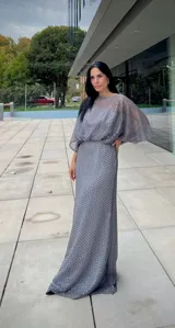 Vestido largo de fiesta color gris, confeccionado en tejido con textura calada tipo red. Presenta un diseño de silueta fluida con mangas amplias tipo murciélago y escote redondo.