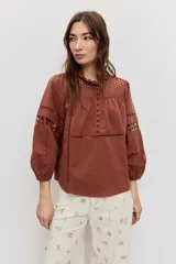 Camisa de manga larga abullonada color marrón, con detalles de bordados calados en el pecho y las mangas, y cierre frontal con botones.