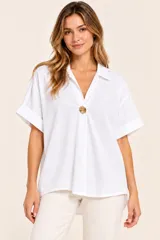 Camisa de algodón blanca con cuello en V, mangas cortas con vuelta y un botón dorado decorativo en el centro.