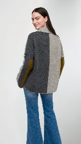 Polera de cuello alto confeccionada en lana lambswool, con diseño bicolor en negro y marrón. Presenta mangas largas con franjas verticales en gris y un parche circular bordado en la manga derecha.