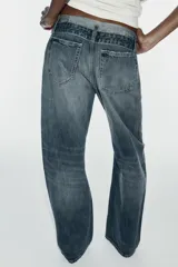 Jeans de mezclilla de tiro medio, corte wide leg y diseño relaxed. Presenta detalles rotos y desgastados en las piernas, y una cinturilla doblada superpuesta con trabillas y cierre frontal con cremallera y botón metálico.