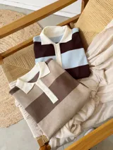 Sweater tipo chomba de tejido bremer con diseño de rayas horizontales en color marrón y celeste. Presenta cuello polo en color crema con cierre frontal de botones y mangas largas.