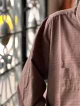 Camisa oversize color marrón con diseño a rayas finas, cuello camisero, manga larga y bolsillo aplicado en el pecho.
