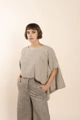 Poncho color beige con diseño a cuadros, cuello bote y terminaciones desflecadas. Tiene aberturas para los brazos en los laterales y detalles en cuero.