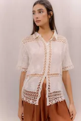 Camisa de algodón color crudo, con cuello camisero, mangas cortas y cierre frontal con botones. Presenta paneles de tejido calado y detalles bordados transparentes.