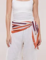 Pañuelo de gasa liviana con diseño estampado de rayas en tonos beige, naranja y azul marino, con detalles geométricos de tiras y herrajes.