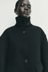 Abrigo corto de paño con mezcla de lana, color negro. Presenta cuello subido con cierre de botones, manga larga y dos bolsillos de plastrón con solapa en el frente. Cierre frontal con botones.