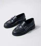 Mocasín de cuero vacuno negro con detalle de pieza de cuero con textura de cocodrilo y hebillas metálicas. Suela de caucho con plataforma.