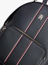 Mochila de poliuretano texturizado en color azul marino, con diseño curvo, bolsillo frontal con cierre y detalles de franjas verticales con los colores distintivos de la marca. Cuenta con el monograma TH metálico en dorado, cierre de cremallera superior, asa de mano y correas ajustables para la espalda.