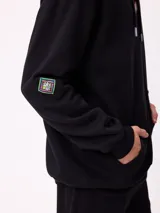 Canguro marrón con capucha y bolsillo frontal, con un diseño gráfico colorido en la espalda que representa una casa surrealista con el texto 'Supreal State of Mind'.