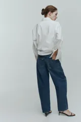 Jean tobillero de cinco bolsillos en denim de algodón rígido, con piernas de volumen curvo, corte estándar y tiro alto con cierre de botones.