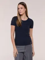 Remera básica de modal elastizado color blanco, con textura acanalada fina, escote redondo y mangas cortas. Presenta un pequeño logo metálico aplicado cerca del ruedo frontal.