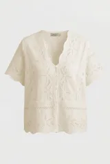 Blusa corta de broderie color crudo, con mangas cortas, escote en V con rebordes ondulados y cierre frontal de botones.