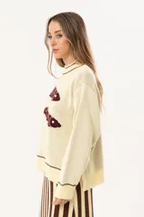Sweater color manteca de tejido de punto con cuello redondo y ribete marrón. Presenta dos peces marrones tejidos en el frente con detalles bordados a mano.