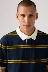 Remera polo de manga corta, color azul marino con rayas horizontales amarillas y verdes. Tiene cuello blanco y tapeta de botones.