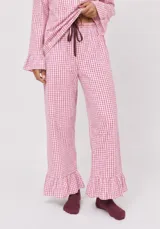 Conjunto de dos piezas de pijama confeccionado en algodón a cuadros vichy rosados y blancos. Incluye una camisa de manga larga con puños acampanados y cierre delantero con cordones para atar, y un pantalón largo de corte recto con volados en el ruedo.