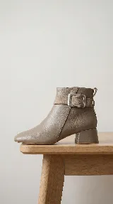 Bota corta de cuero con taco cuadrado bajo y punta redondeada. Presenta una tira decorativa en el tobillo con una hebilla metálica rectangular. Cuenta con cierre lateral interno para facilitar el calce.