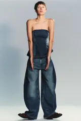 Jeans de tiro alto, color azul medio lavado, con un corte extremadamente ancho y voluminoso (balloon/oversize). Presenta costuras torcidas y paneles de denim de tono ligeramente diferente en los laterales, creando un efecto visual dramático.