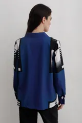 Camisa de manga larga con cuello solapa y cierre frontal de botones. Presenta un diseño estampado con bloques geométricos en tonos azul, blanco y negro.