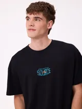 Remera de corte oversize color crema con estampado gráfico en la espalda que muestra un oso, un paisaje natural y el texto 'Stay close to the source'.