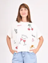 Remera blanca de manga corta y cuello redondo, con estampado gráfico que incluye corazones, copas de vino, labios, un leopardo y texto en italiano como "Amore" y "Salute!!".