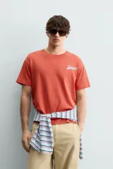 Camiseta de corte relajado con cuello redondo y manga corta. Presenta un estampado frontal con texto en contraste y un acabado con efecto lavado que le otorga una apariencia única.