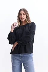 Blusa de manga larga color negro, confeccionada en 100% algodón con textura bordada. Presenta detalles de tablas en el frente y en los puños, con un corte holgado y cuello redondo con pequeña abertura.