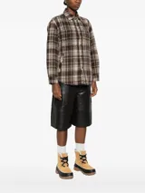 Sobrecamisa de franela con diseño a cuadros en tonos marrón oscuro, beige y blanco. Presenta un calce holgado, cuello camisero, cierre frontal de botones y bolsillos en el pecho.