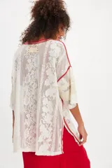 Remera oversize de inspiración deportiva en malla de encaje color blanco, con terminaciones en rojo, franjas estilo varsity en las mangas, escote redondo, hombros caídos y aberturas laterales en el ruedo.