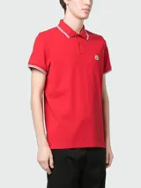 Remera polo Moncler confeccionada en piqué de algodón color rojo, con cuello y puños acanalados con líneas blancas y detalle de parche con logo en el pecho.
