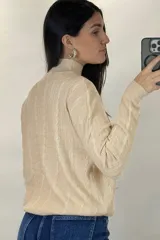Buzo de hilo de punto con diseño de trenzas verticales, cuello alto y cadena metálica decorativa incorporada en la parte frontal.