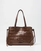 Cartera de mano tipo tote color marrón con textura símil cocodrilo, doble asa de hombro y detalles de tiras colgantes en los laterales.