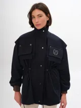 Trench azul marino con cuello alto, cierre frontal de botones a presión y cordón ajustable en la cintura. Presenta cuatro bolsillos frontales con solapa y un parche con el logo de la marca en el pecho.