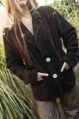 Blazer de gamuza color marrón oscuro, con solapas de muesca, cierre frontal de dos botones grandes claros y bolsillos frontales ribeteados.