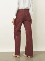 Jean de corte recto y tiro medio en color bordeaux, con detalle de tachas metálicas a lo largo de las costuras laterales y ruedo desflecado.