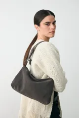 Cartera de hombro mediana confeccionada en cuero agamuzado color gris, con cierre superior y correa ajustable mediante hebilla metálica.