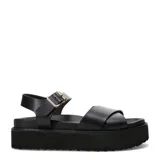 Sandalias Miss Carol modelo Marbela, de color negro con plataforma flatform recta y suela con relieve texturizado. Capellada con tiras anchas cruzadas sobre el empeine y correa trasera con hebilla metálica dorada para ajuste seguro.