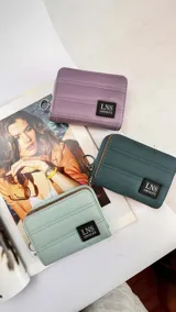 Billetera corta de diseño capitoneado con cierre perimetral y solapa frontal. Cuenta con compartimentos internos para tarjetas y billetes, e incluye una correa de mano desmontable.