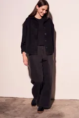 Sobrecamisa negra de estilo shacket, confeccionada en tejido de gamuza sintética. Presenta cuello camisero, cierre frontal de botones y dos bolsillos de parche con solapa en el pecho. El calce es oversize y las mangas son largas.