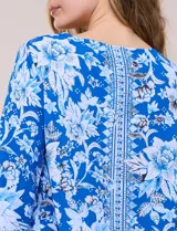 Blusa de gasa azul con estampado floral y geométrico estilo pañuelo, escote redondo, mangas tres cuartos amplias con jareta ajustable y ruedo asimétrico en punta.