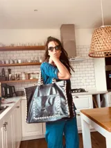 Bolso tipo tote de cuero negro con bolsillo externo y llavero interno. Tiene manijas cortas con diseño chevron y costuras blancas a contraste.