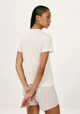 Pijama de algodón compuesto por una remera blanca de manga corta con inscripción frontal y un short a rayas en tonos salmón y beige con cintura elástica.