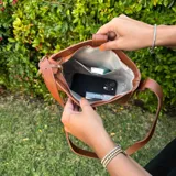 Cartera tipo morral de eco cuero color marrón, con cierre superior y correa larga ajustable. Interior forrado con bolsillos organizadores.