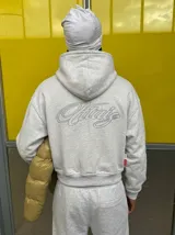 Hoodie gris melange con capucha, cierre frontal y gran bordado en relieve en la espalda.