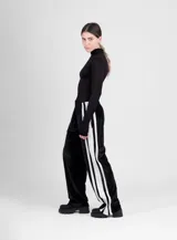 Pantalón de terciopelo negro de corte ancho, con cintura elástica y tres rayas blancas verticales en los laterales.