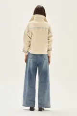 Campera de lana merino hervida en color crudo, con diseño de cuello camisero, cierre frontal de botones y bolsillos frontales. Presenta bordados artesanales con motivos geométricos en tonos marrón y azul en el frente, espalda y mangas.