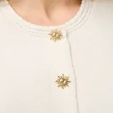 Top sin mangas de punto color beige, con cuello redondo y cierre frontal con botones dorados ornamentados.