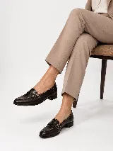 Mocasines de cuero marrón oscuro, con taco bajo, costuras visibles en contraste y detalle de aplique en cuero con grabado croco en el empeine con una hebilla metálica decorativa.