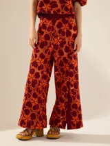 Pantalón de tiro alto y pata ancha con estampado floral en tonos naranja y borgoña. Presenta cintura de tela a tono con abertura lateral con cierre niquelado y tajos en el centro delantero.